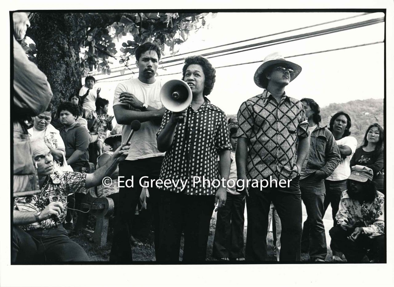 After the circuit court protest demonstration, Waiahole-Waikane residents gather to "sum-up" the protest. With the bull horn is Auntie Nene Manalo, Peter Thompson behind and Bob Nakata on the right. Negative: 2981-4 | Ed Greevy Photographer